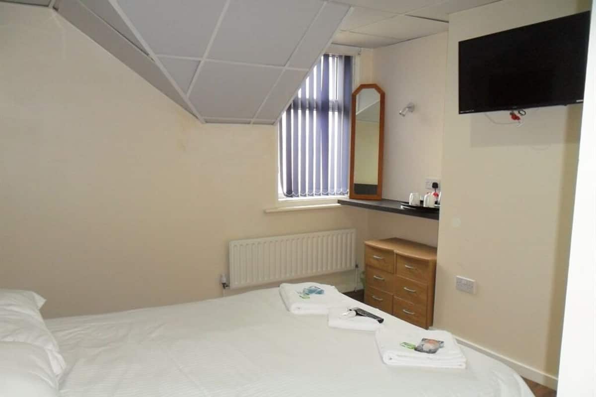 A hotel room with a bed, a dresser, a mirror, a TV, and a window with blinds.
