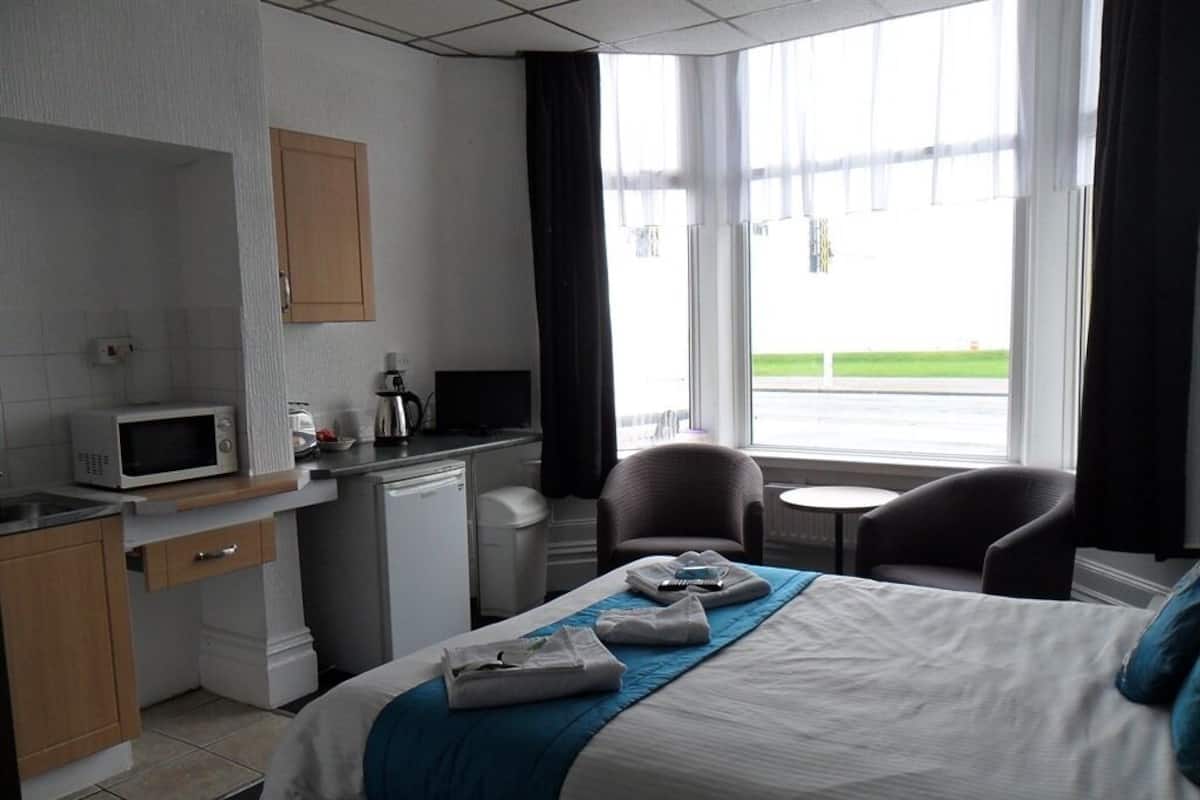 A hotel room with a bed, a desk with a microwave, a coffee maker, and a small table with chairs.