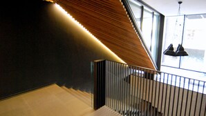 Ein modernes Interieur mit schrägen Wänden, einer Treppe mit Metallgeländer und Blick ins Freie durch große Fenster.