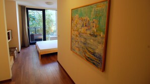 Ein Zimmer mit einem Bett, einem Gemälde und einem Balkon mit Blick auf Bäume.