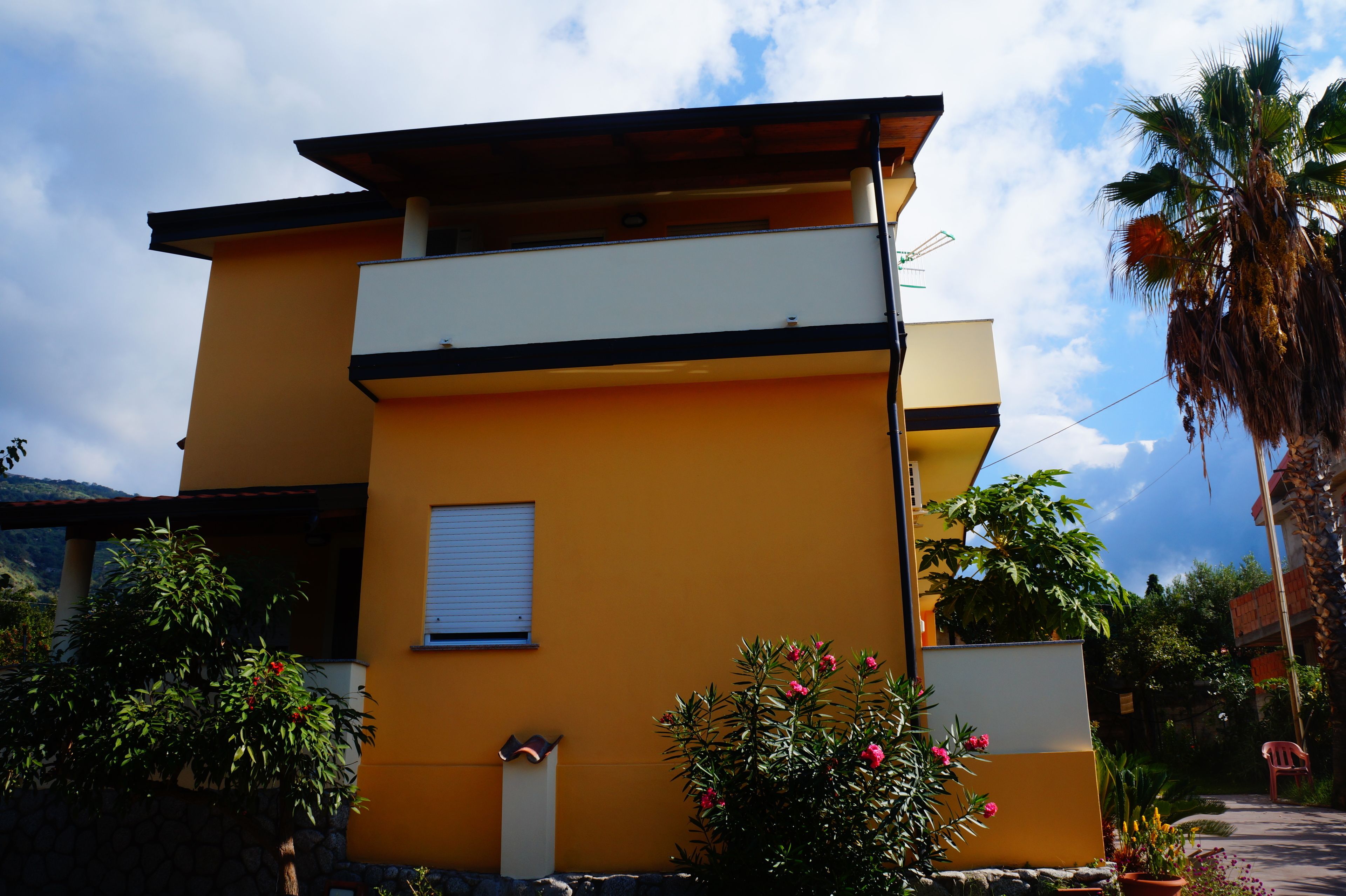 Ein modernes, zweistöckiges Gebäude mit gelber Fassade, einem Balkon und einem kleinen Fenster.