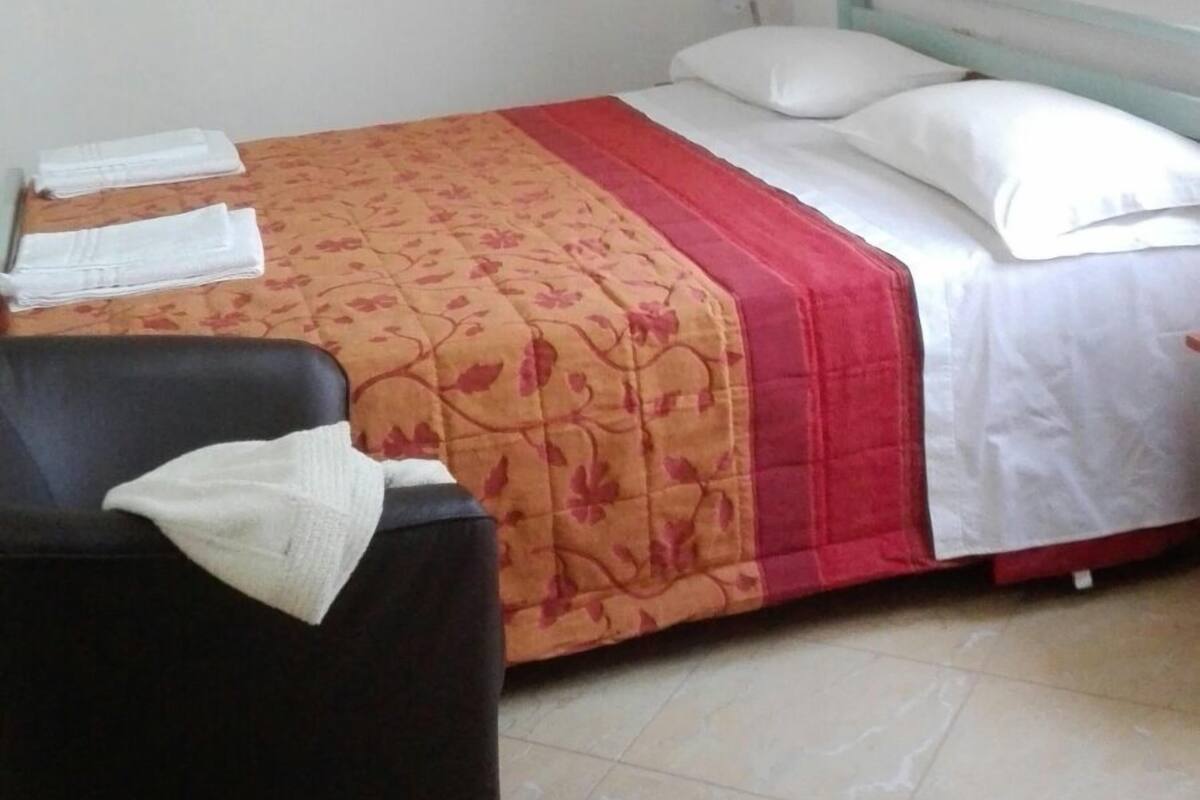 A single bed with a red and white bedspread, a black chair, and a white pillow on the bed.