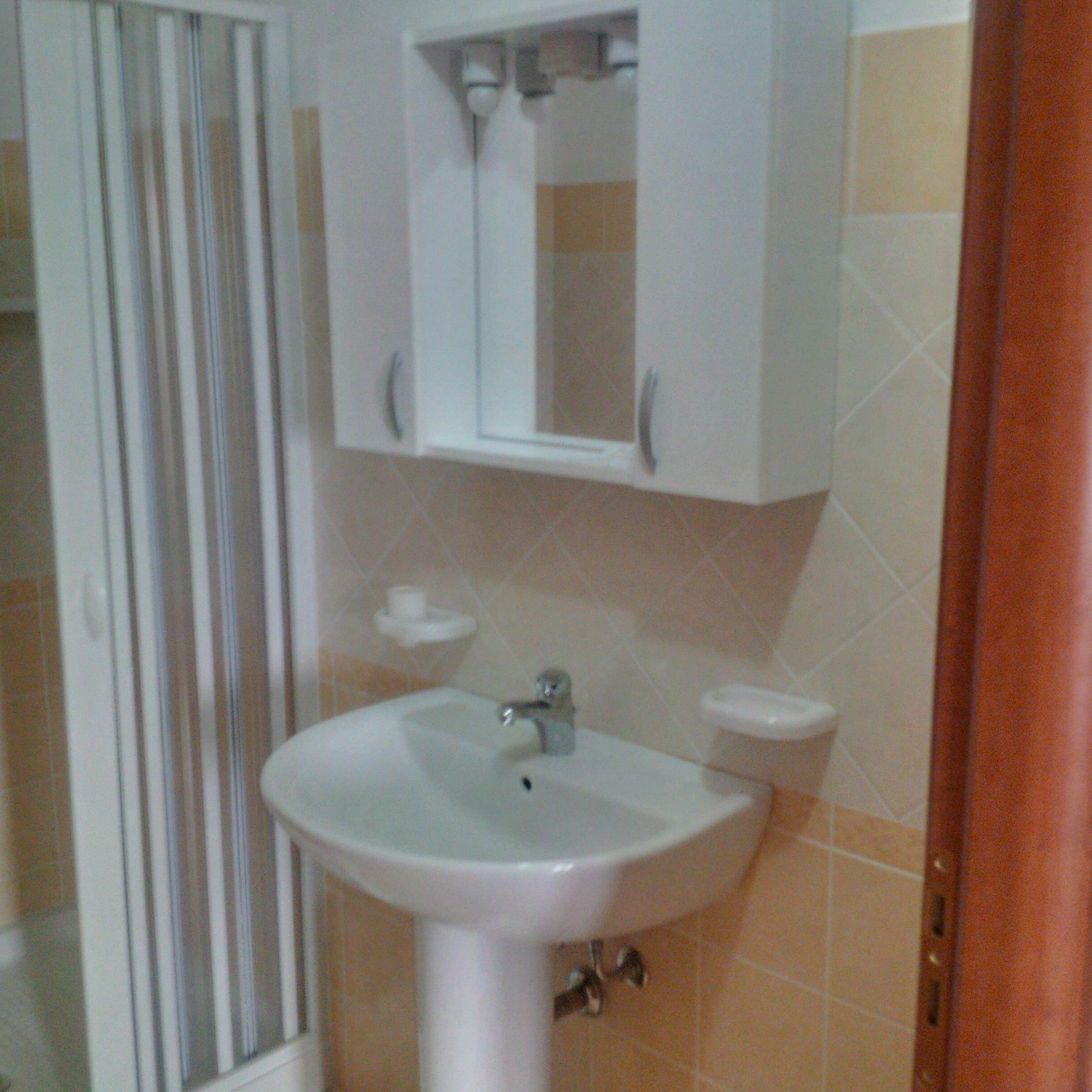Un baño con lavamanos blanco, un espejo encima y un inodoro.