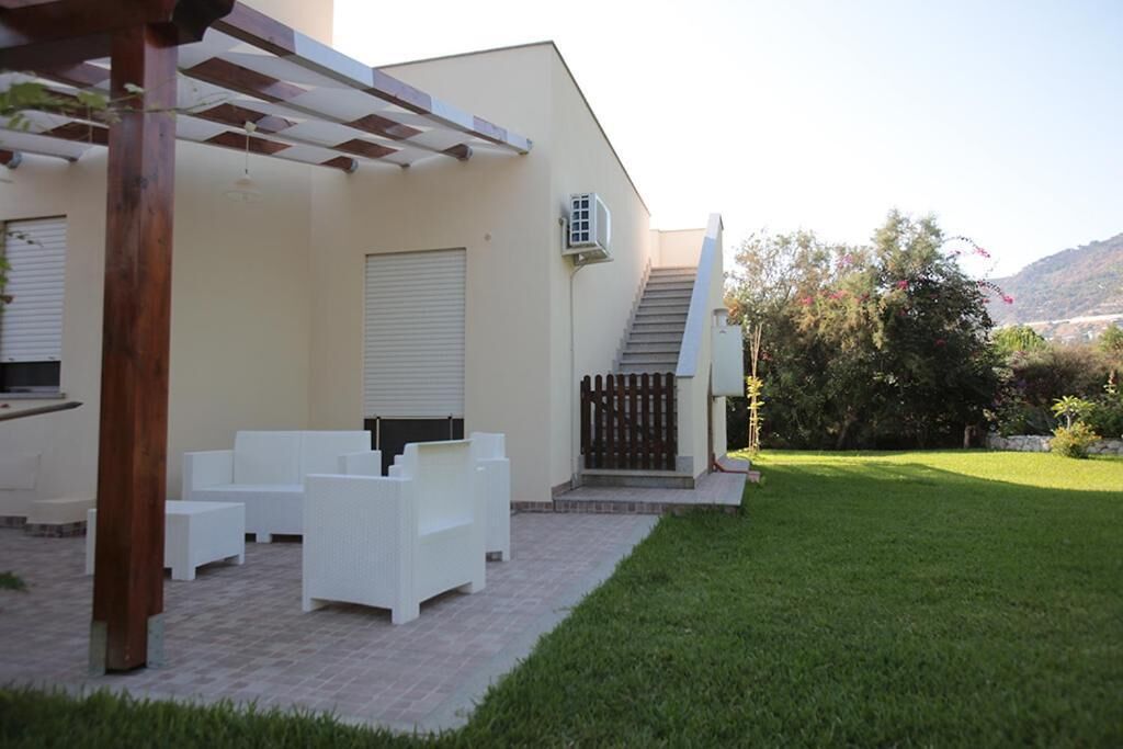 A covered patio with white furniture, a wooden pergola, and a view of a hillside.