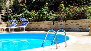 Une piscine avec deux chaises longues à rayures bleues et blanches et un mur de pierre orné de fleurs colorées.