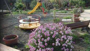 Ein Spielplatz mit Rutsche und Karussell, umgeben von Topfpflanzen und einer Bank.
