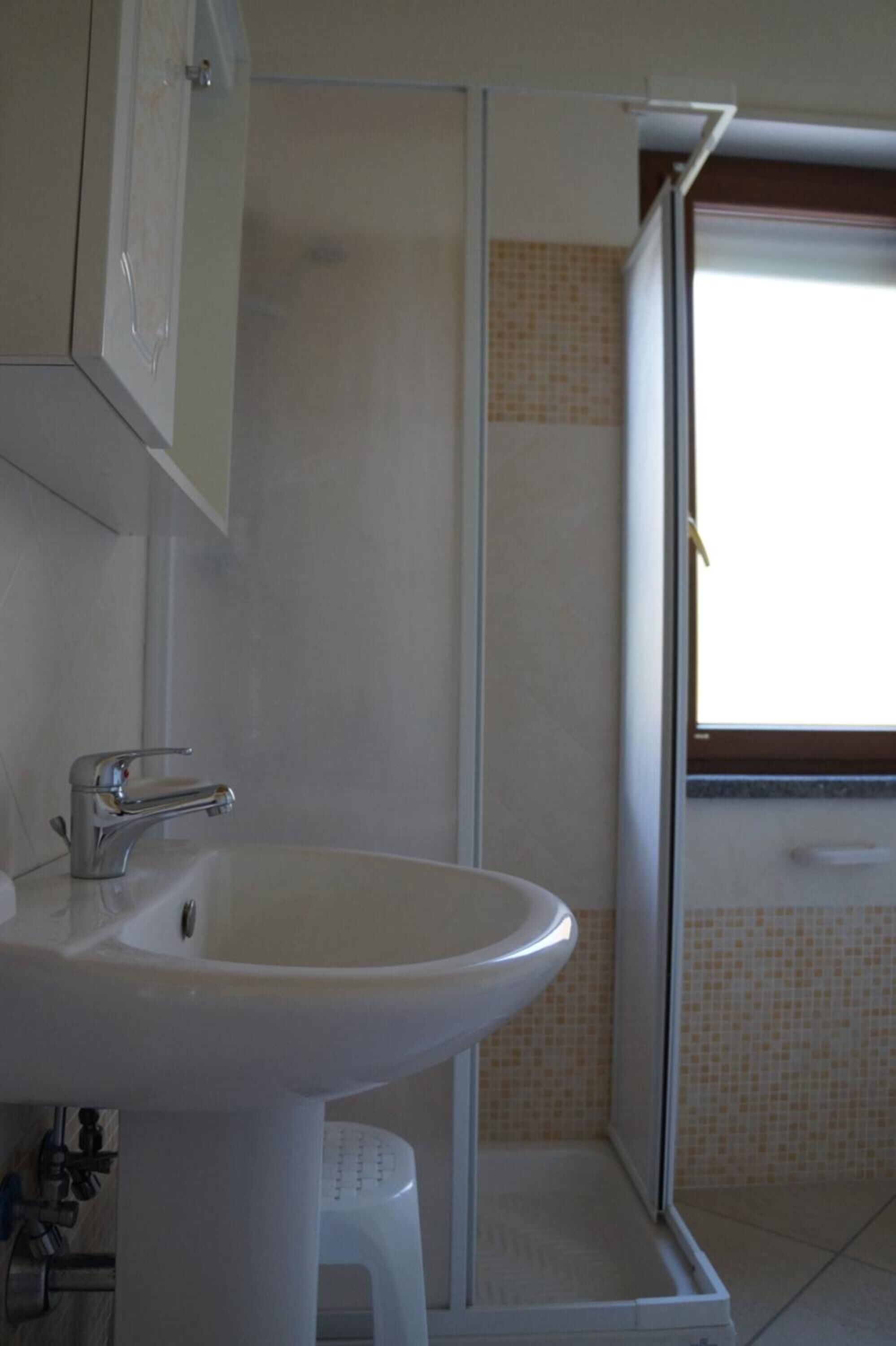 A bathroom with a white sink, a glass shower enclosure, and a window providing natural light.