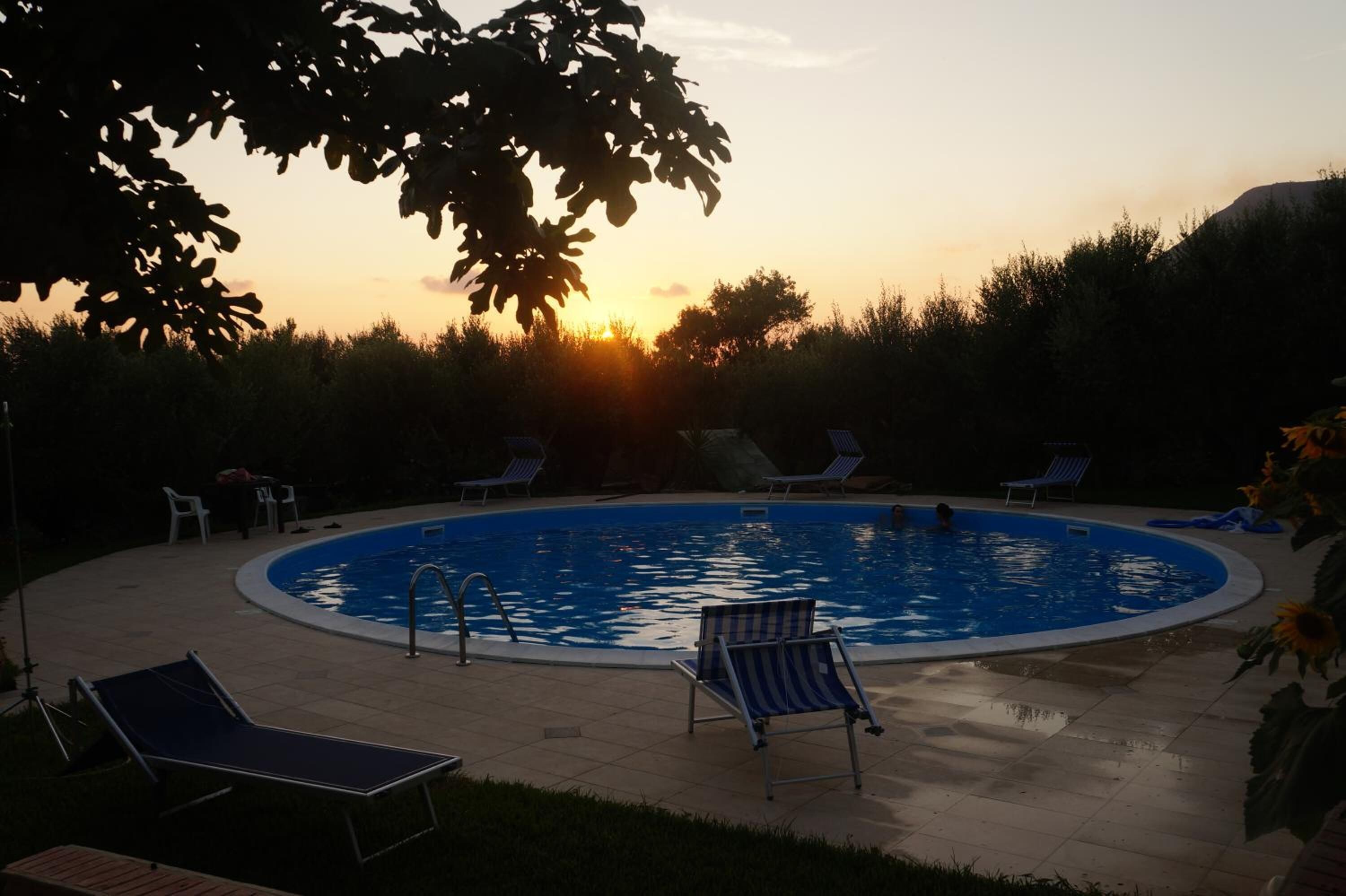 Une piscine ronde entourée de chaises longues, le tout mis en valeur par le décor d’un coucher de soleil.