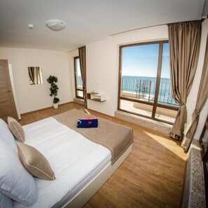 Een hotelkamer met een bed, een tafeltje, een plant en uitzicht op zee.
