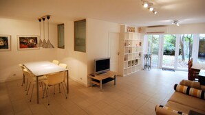 Uma sala de estar com uma mesa de jantar, cadeiras, televisão e sofá.