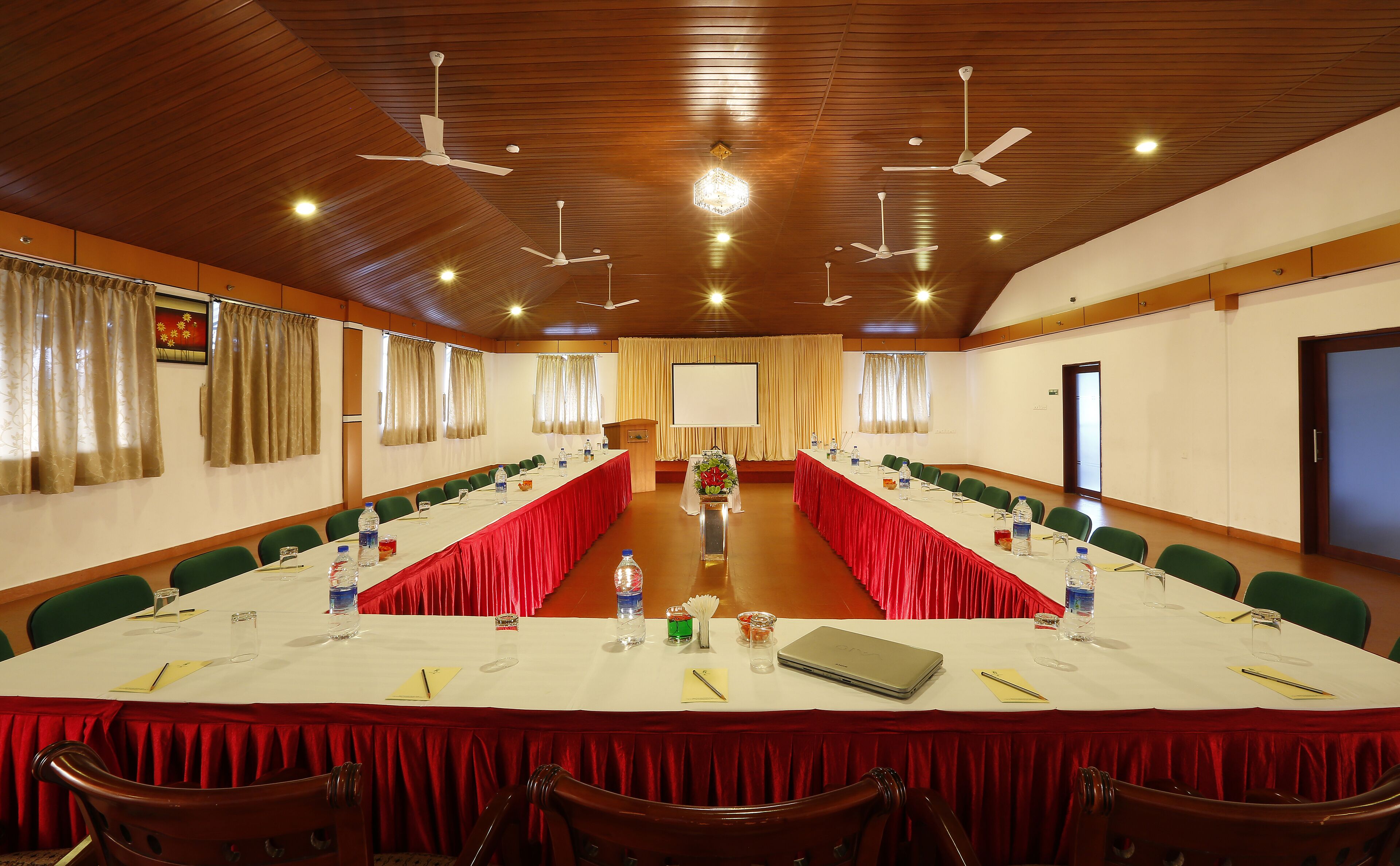 A conference room with a long table, chairs, a podium, and a screen.