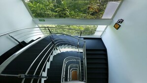 A modern interior with a glass ceiling, a staircase, and a view of lush greenery outside. - Spicegrove (Udumbanchola)