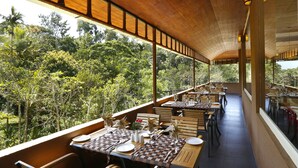 An outdoor dining area with tables set for two, overlooking a lush forest. - Spicegrove (Udumbanchola)