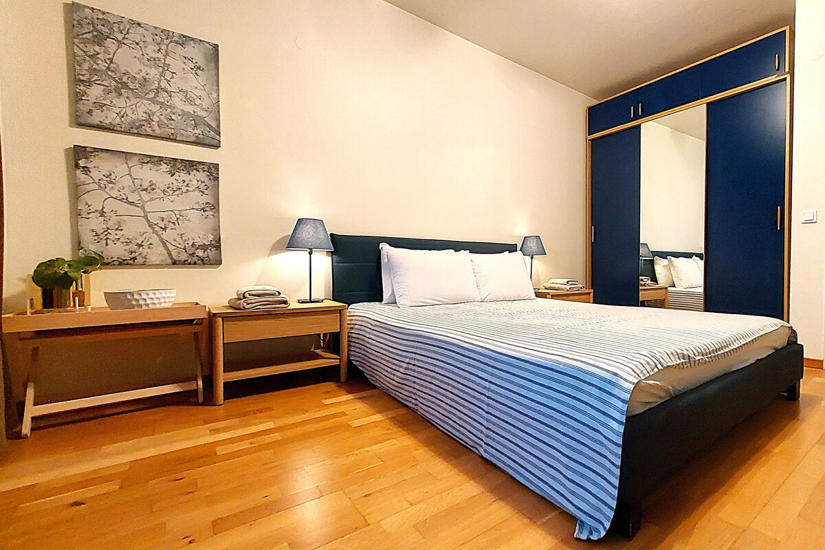 Una habitación de hotel con una cama, mesitas de noche, lámparas, un espejo y un armario.