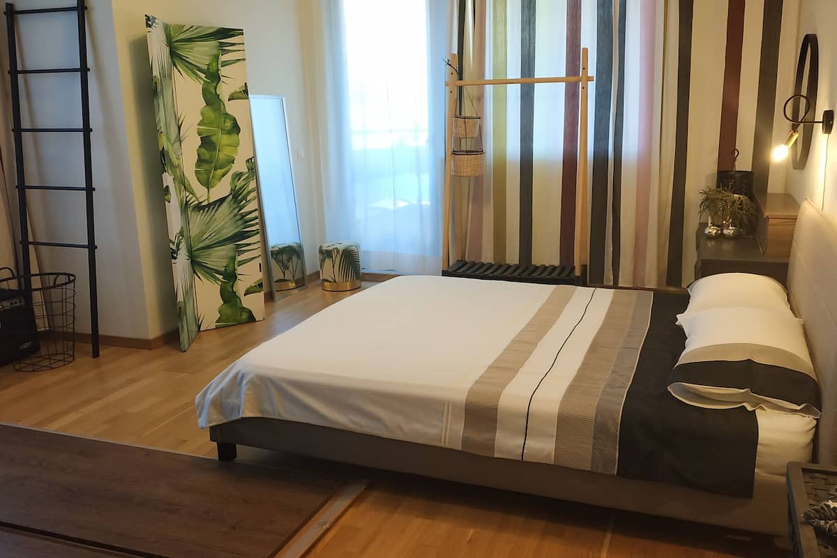 A modern bedroom with a bed, a ladder, a plant, and a wall-mounted light fixture.