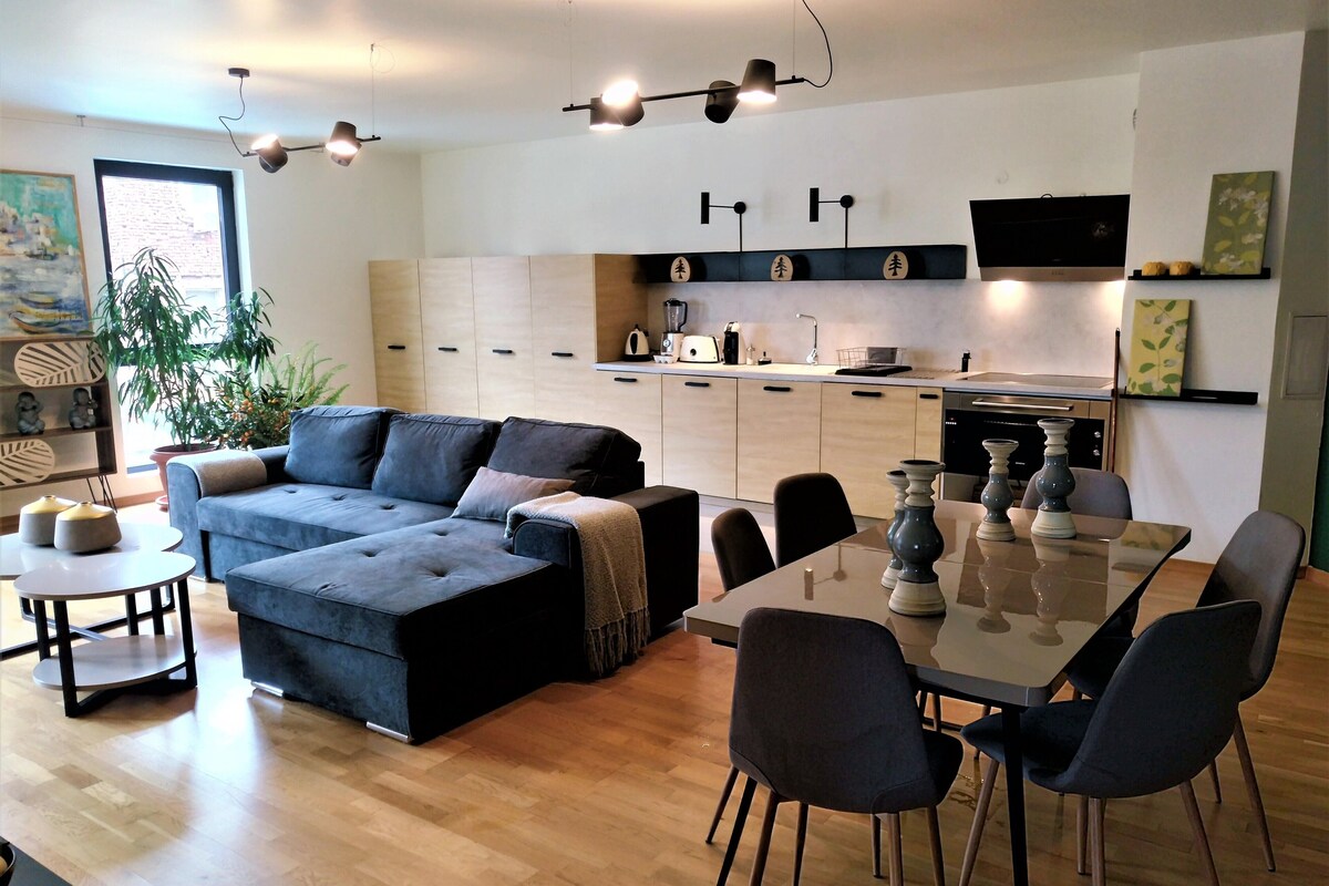 Una sala de estar moderna con sofá, mesa de comedor, sillas y una cocina con armarios y electrodomésticos.