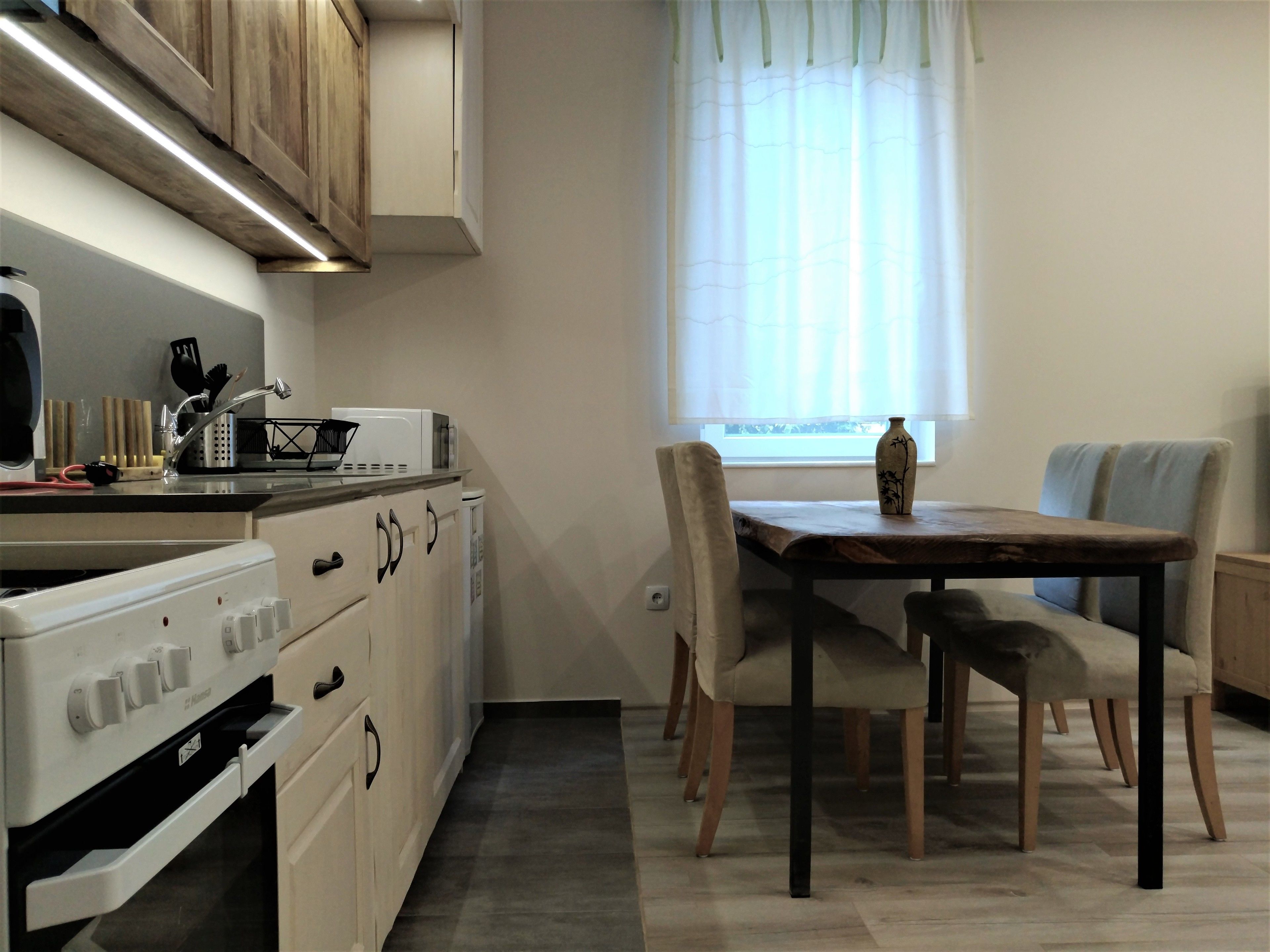 Una cocina con armarios blancos, una estufa y un microondas. Hay una mesa de comedor con sillas y un florero encima.