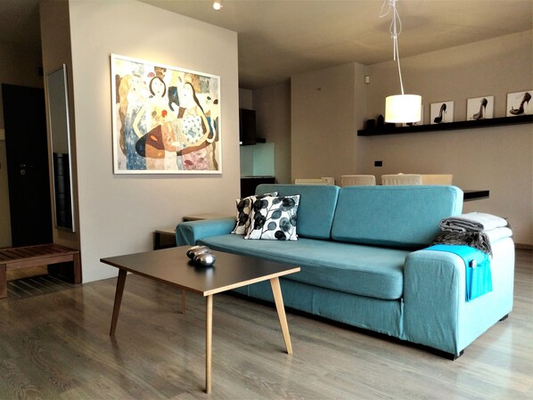 Una sala de estar moderna con un sofá azul, una mesa de centro de madera y un cuadro abstracto grande en la pared.
