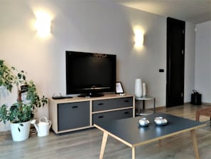 Una sala de estar moderna con un televisor de pantalla plana, una mesa de centro, una planta en maceta y una mesita auxiliar con un florero.