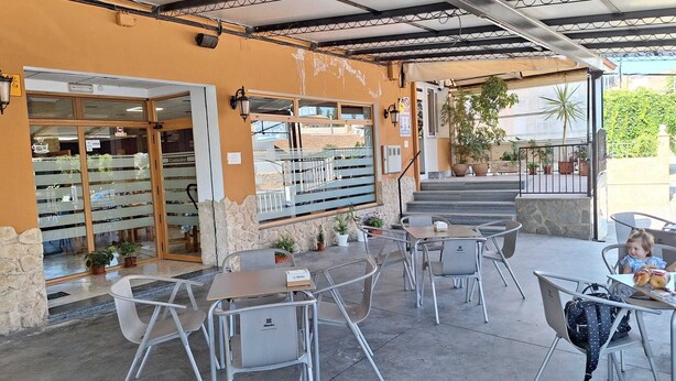 Un café en plein air avec des tables et des chaises, un escalier menant à un niveau supérieur et des plantes en pot.