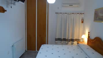 A bedroom with a bed, a bedside table with a lamp, a wardrobe, a radiator, and a ceiling light.