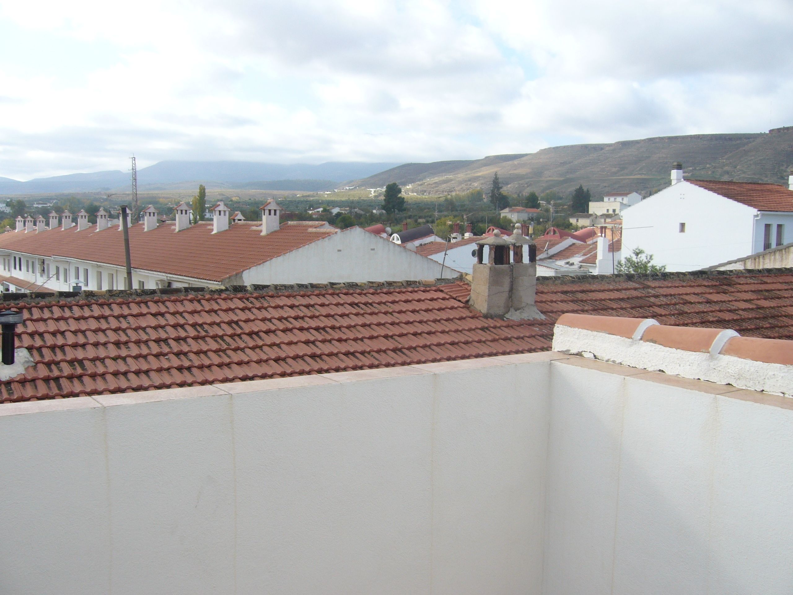 Un barrio residencial con tejados de tejas color terracota, edificios blancos y un paisaje montañoso al fondo.