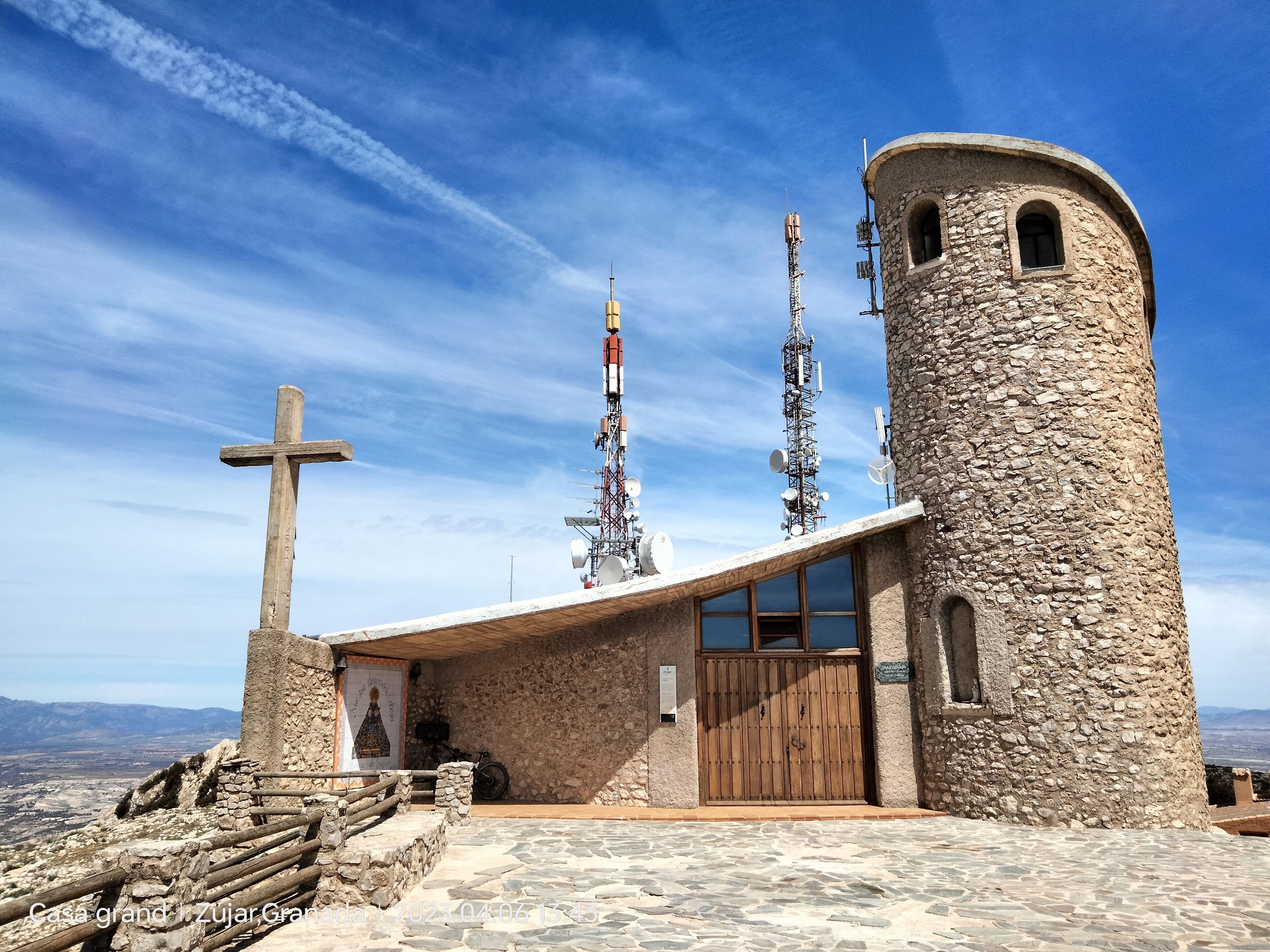 A stone building with a wooden door and a cross, surrounded by a stone wall and a wooden fence.