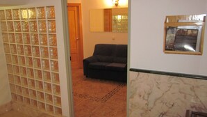Un couloir avec une cloison en verre, un canapé noir et un mur en marbre orné d’une plaque.