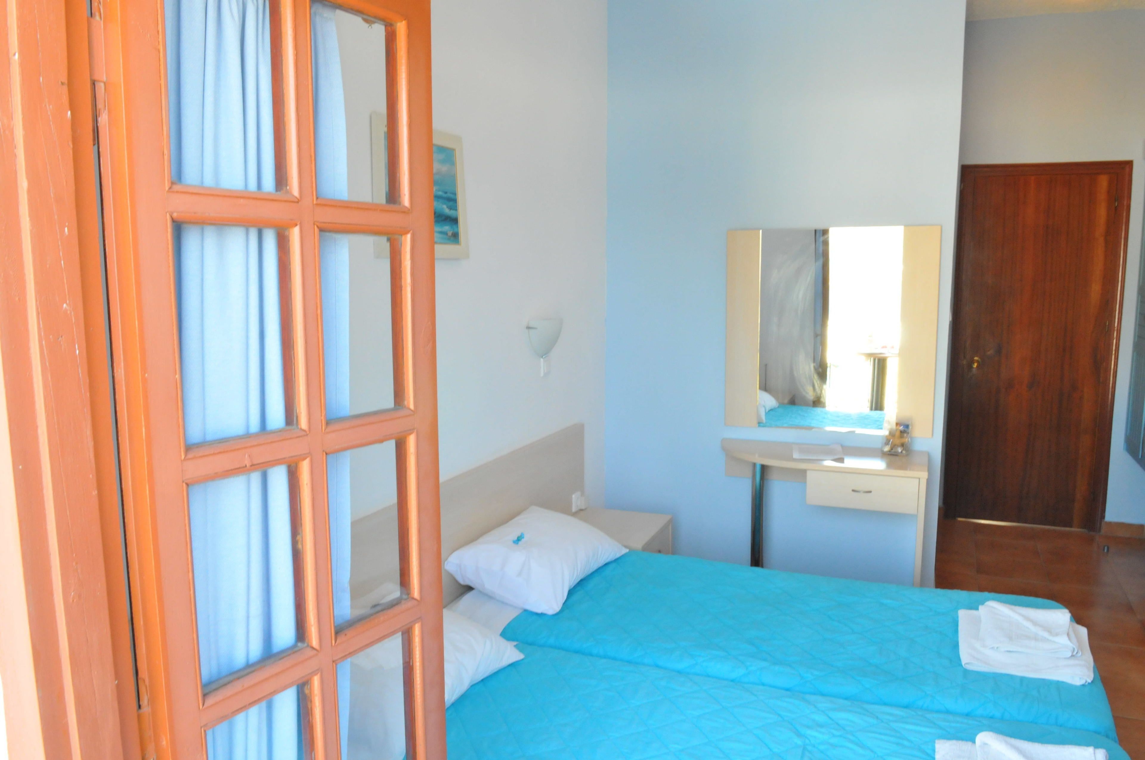 A bedroom with a bed, a nightstand, a mirror, a wooden door, and a window with curtains.
