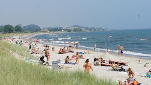 Una playa concurrida, gente tomando el sol y nadando.