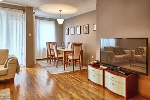 A living room with a dining area, wooden flooring, a sofa, a TV, and a coffee table. - Baratero City Corner II Apartment (Sofia)