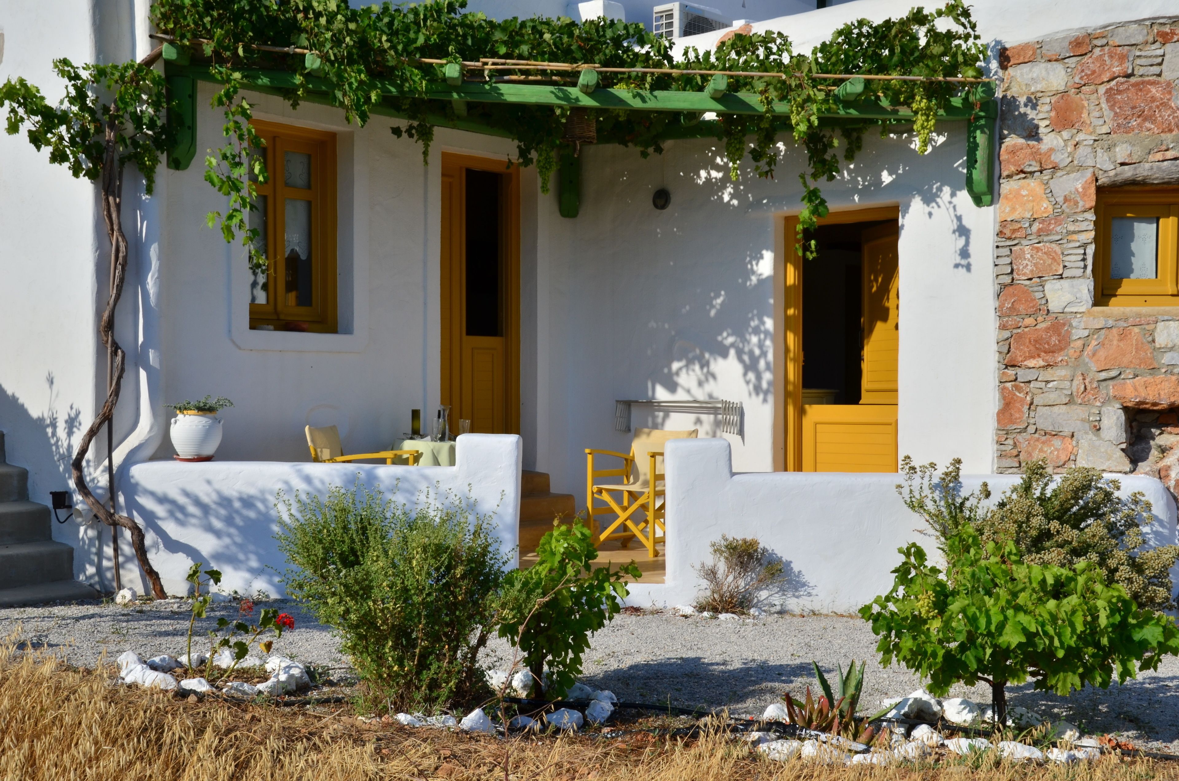 A white building with yellow doors and windows, a stone wall, and a garden with plants and rocks.