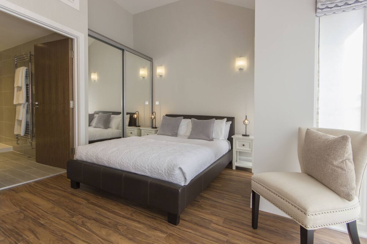 Une chambre moderne avec un grand lit, un miroir, des lampes de chevet et un fauteuil.