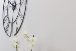 A wall-mounted clock with Roman numerals and a white orchid arrangement.