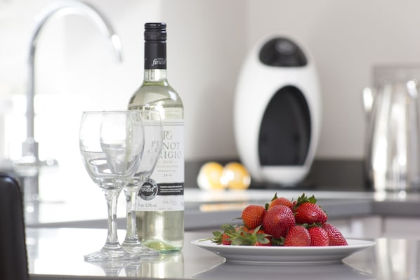 Una encimera de cocina con una botella de vino Pinot Grigio, dos copas de vino y un plato de fresas.