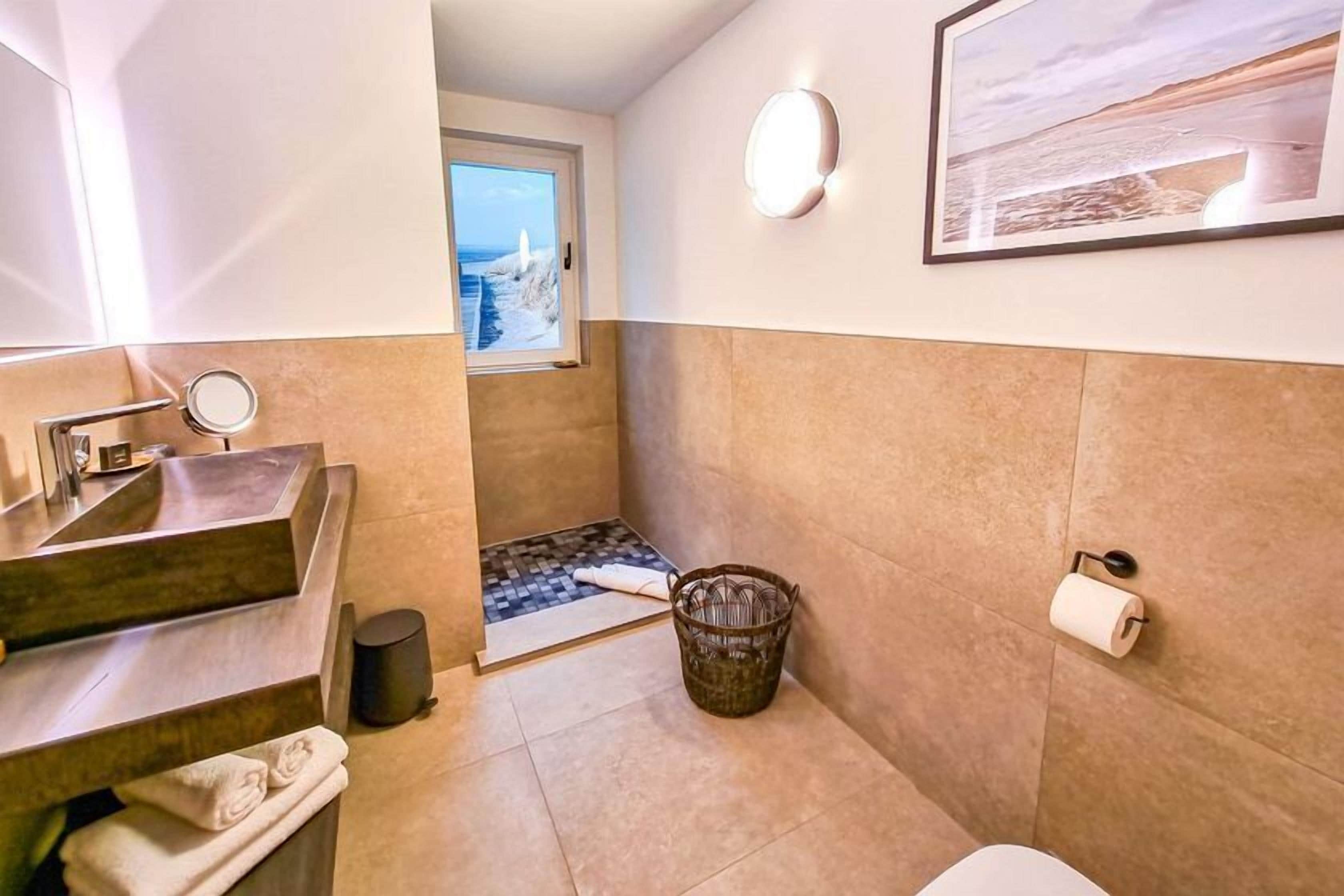 A bathroom with a sink, mirror, and a window with a view of the beach.