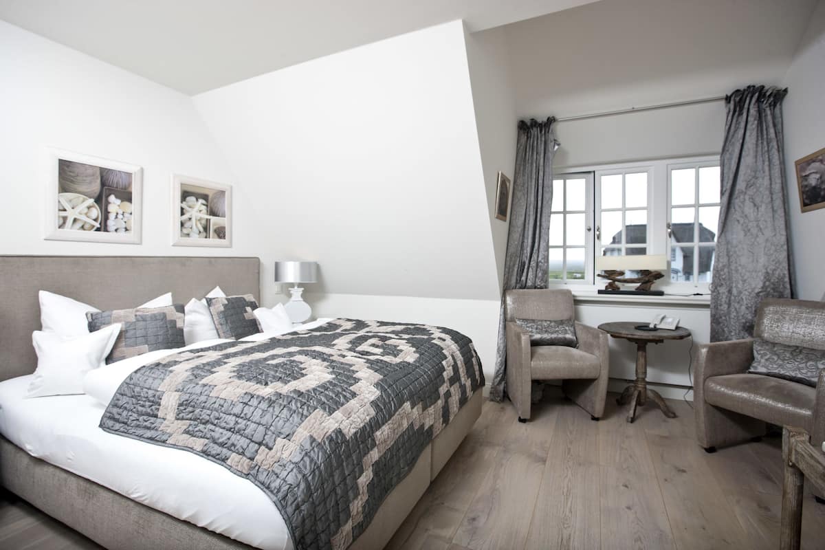 A bedroom with a large bed, two chairs, a small table, and a window with curtains.