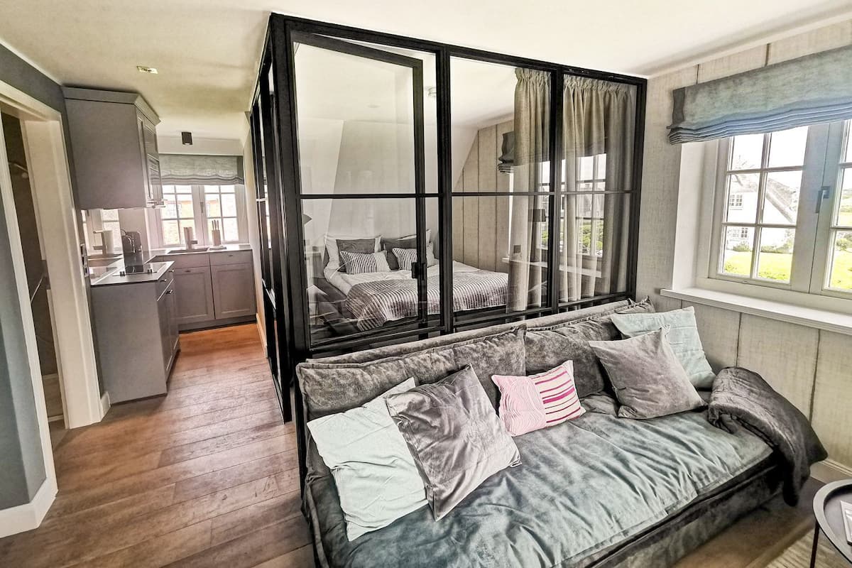 A cozy room with a large window, a sofa, and a view of a kitchen.