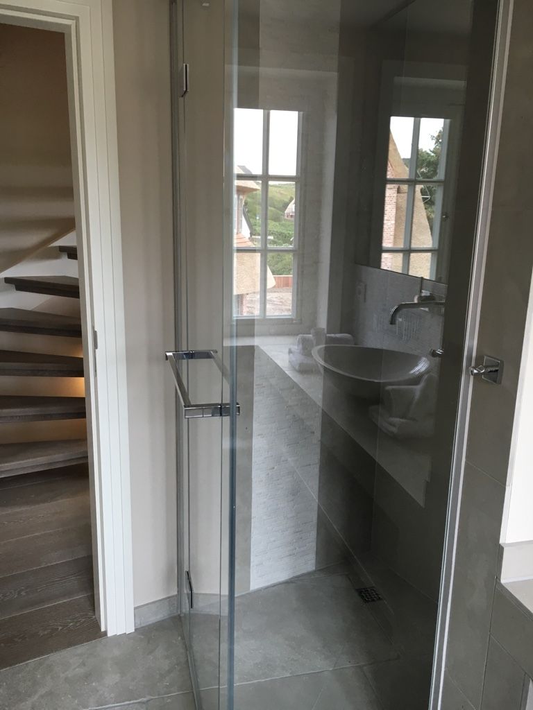 A modern bathroom with a glass shower enclosure, a sink, and a view of a staircase.