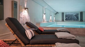 A modern spa area with two lounge chairs, a stone wall, a small pool, and a large framed picture on the wall. - Strandvogtei Sylt (Sylt)