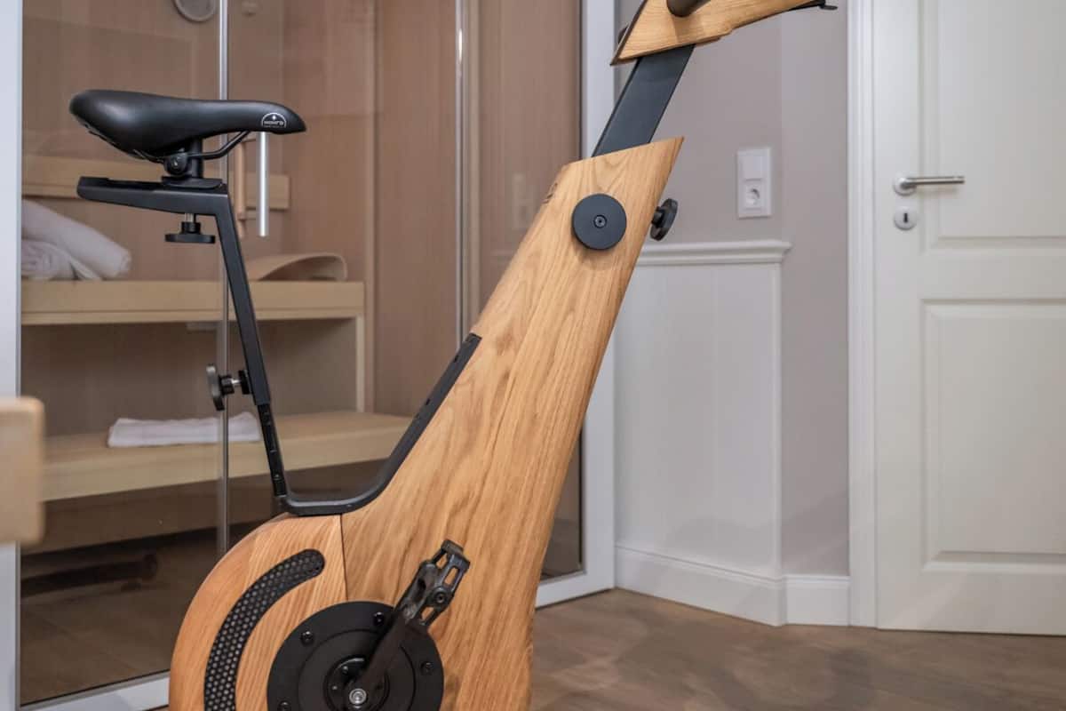 A stationary exercise bike in a room with a wooden floor, a white door, and a sliding glass door leading to a bathroom.