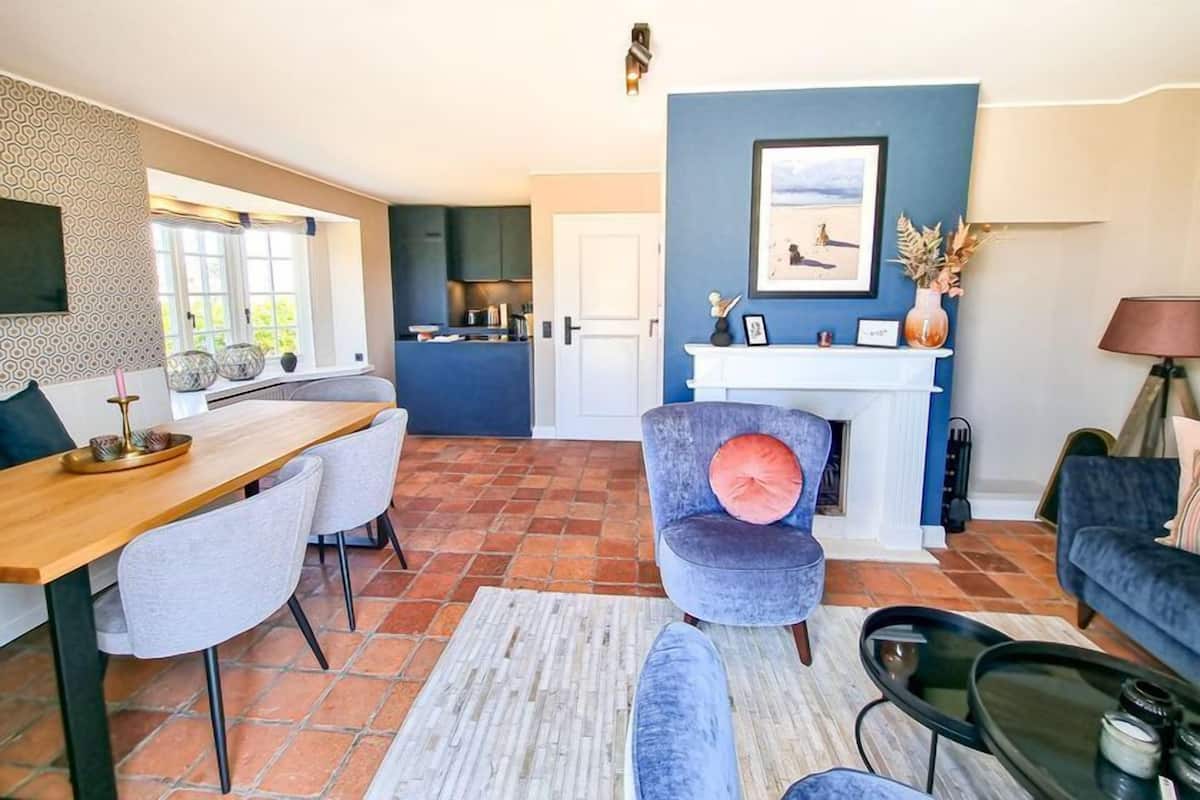 A modern living room with a dining area, a kitchen in the background, and a fireplace.