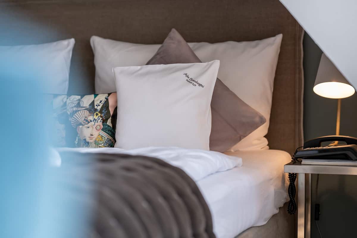 A neatly made bed with white and gray pillows, a bedside lamp, and a phone on a small table beside the bed.