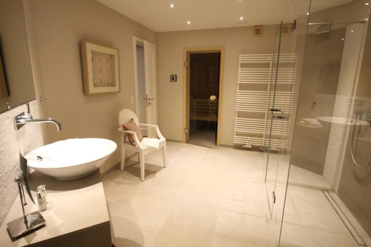 A modern bathroom with a large oval sink, a glass shower enclosure, and a white chair.