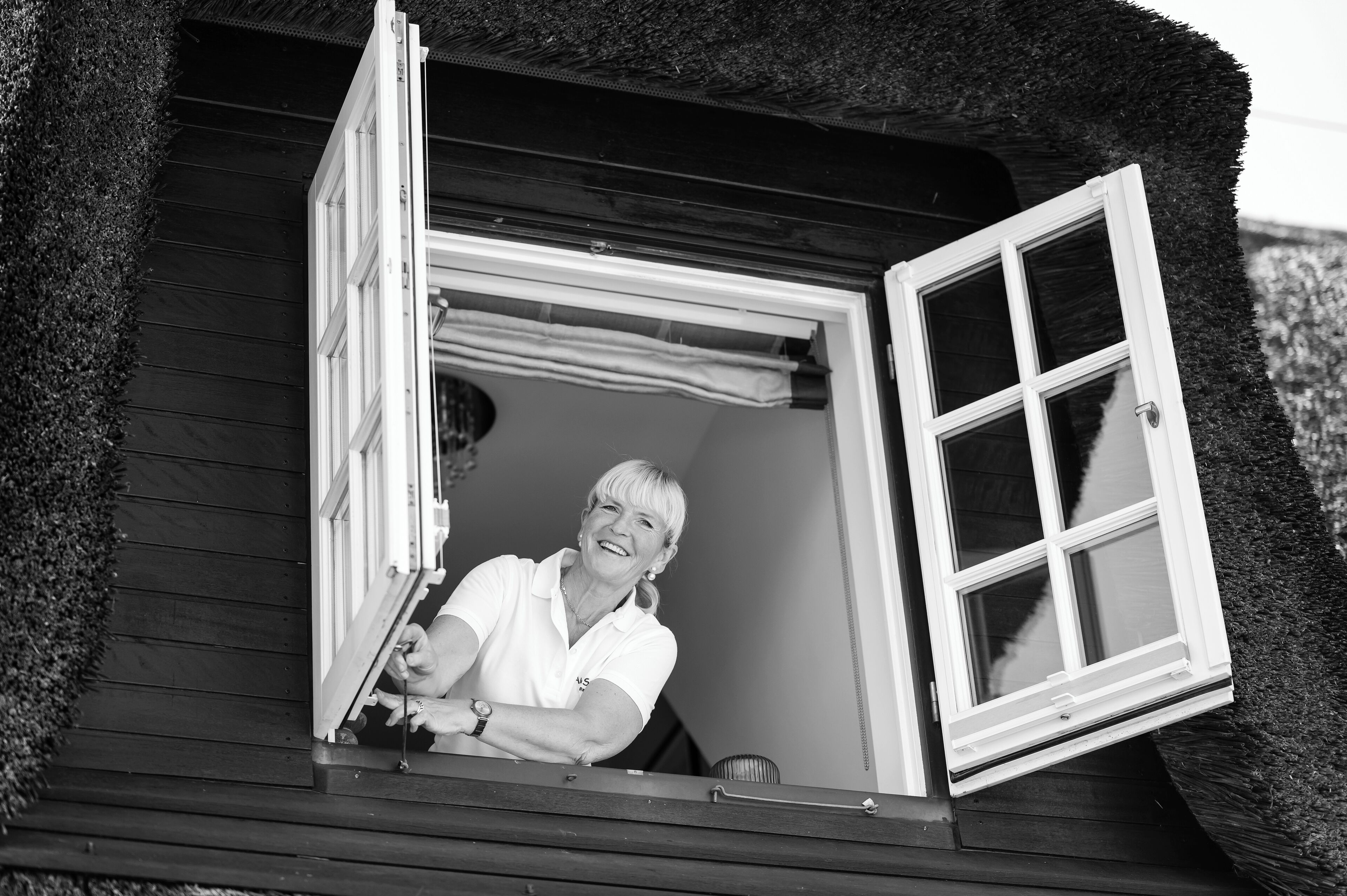 A wooden cottage with a window open, revealing a person inside.