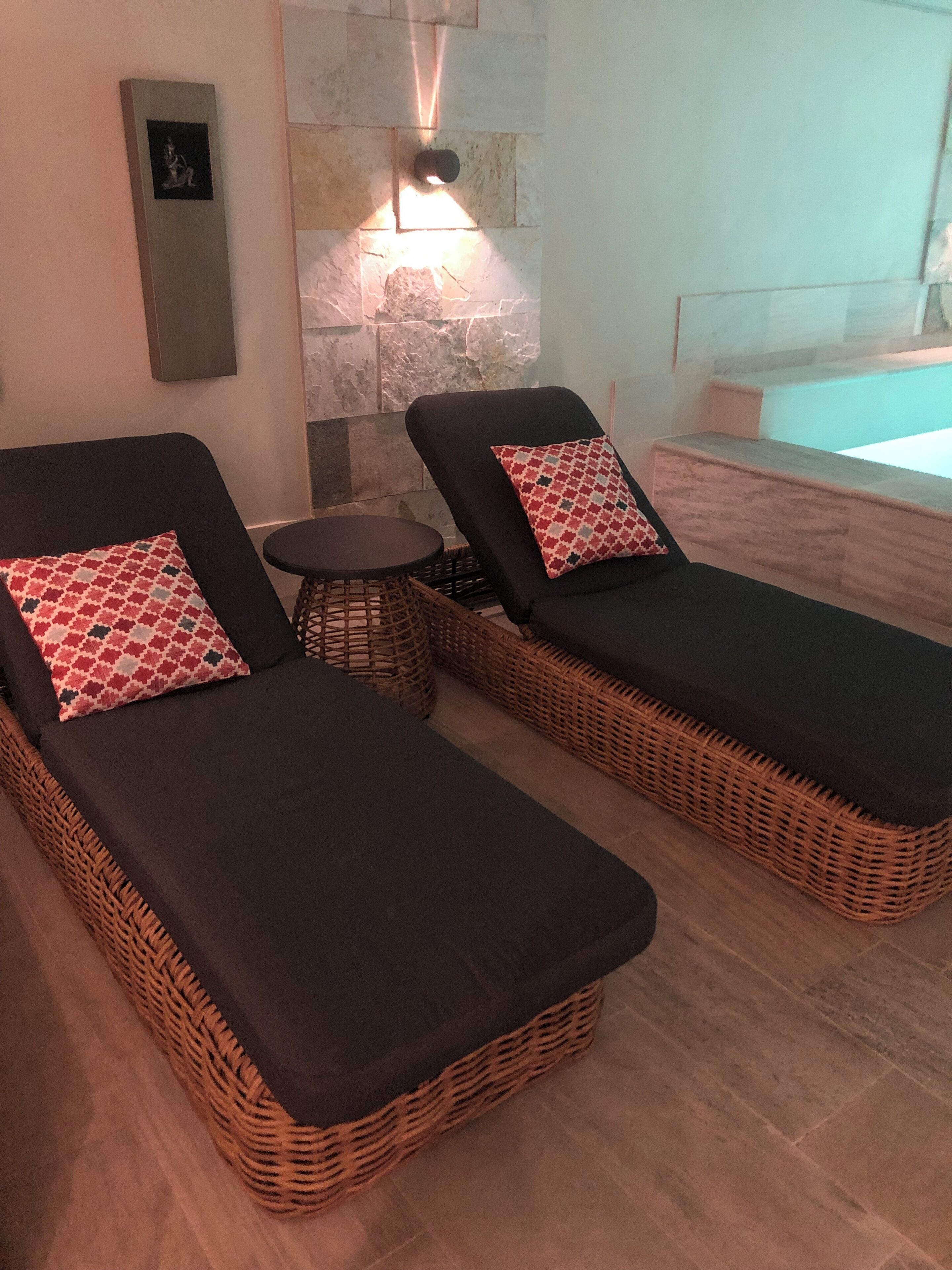 Two lounge chairs with patterned pillows, a small round table, and a stone wall with a light fixture.