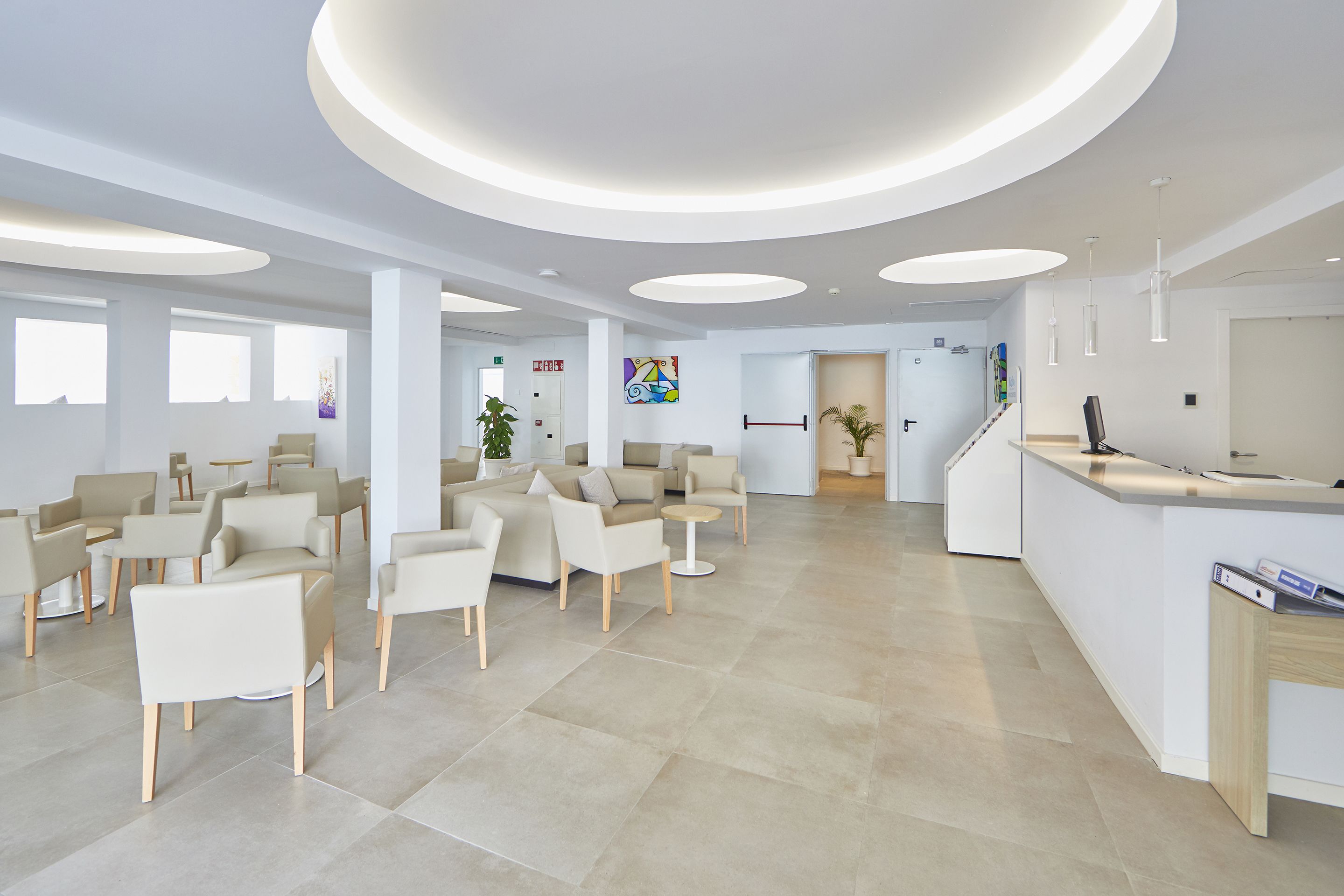 Un área de recepción moderna con un mostrador central, asientos y una escalera que lleva a otras plantas.