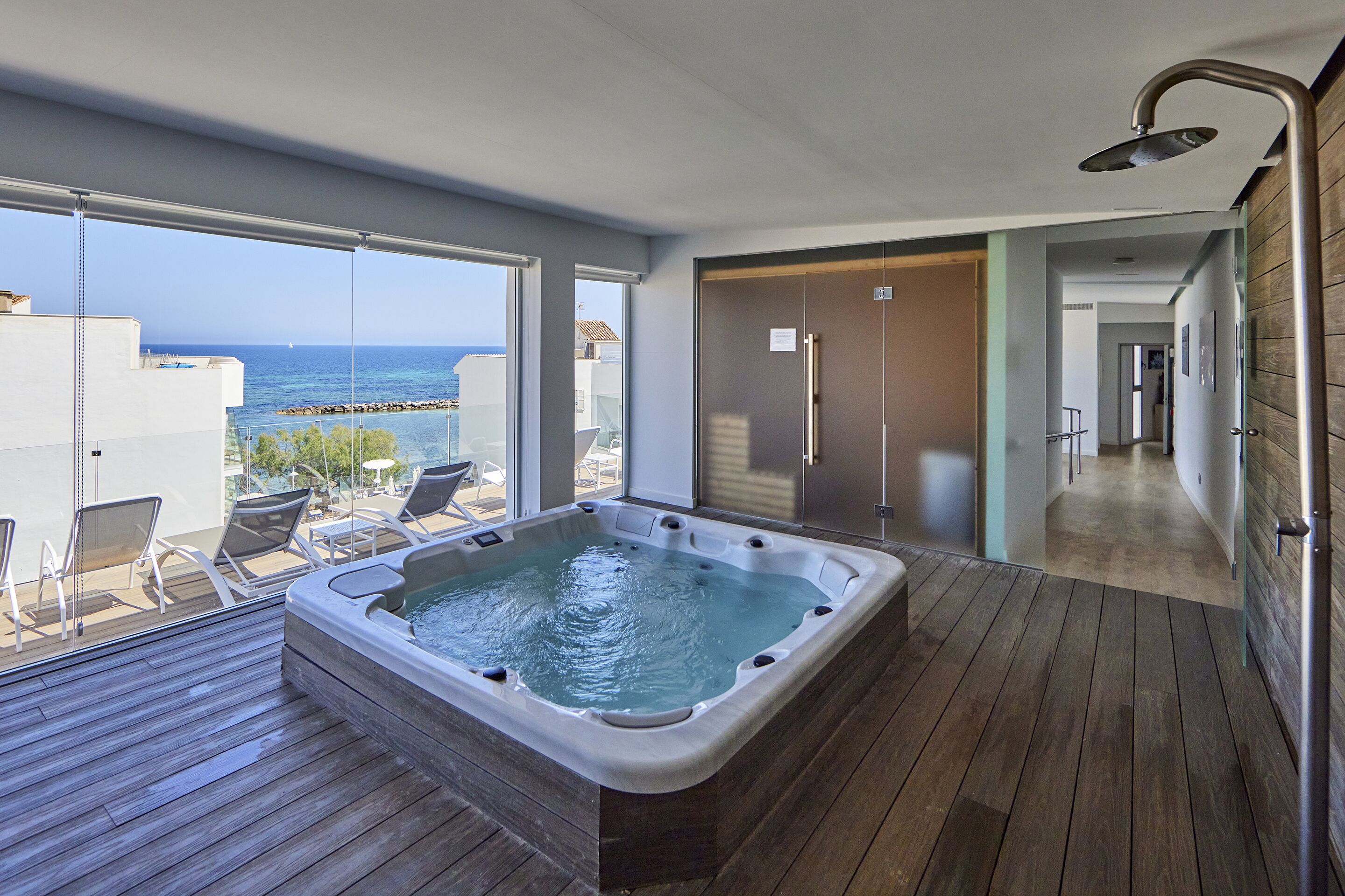 Une salle de bain moderne avec un plancher en bois, une grande baignoire et une vue sur la mer grâce à de grandes fenêtres.