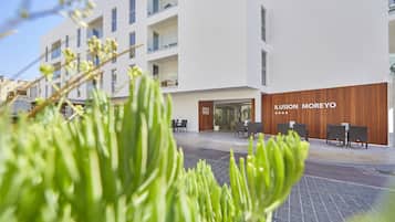 Een modern gebouw met een witte gevel en een houten accentmuur. De naam "ILUSION MOREYO" is op het gebouw te zien.