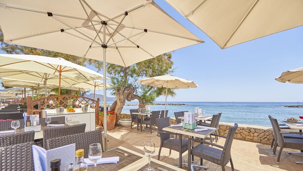 Un área de comedor al aire libre con muebles de mimbre, sombrillas blancas y vistas al mar.